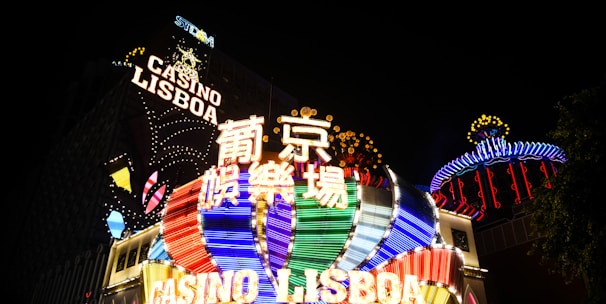 Bright neon signs in multiple colors illuminate the night, prominently displaying the name 'Casino Lisboa' alongside signage in Chinese characters. The lights form intricate patterns and vibrant displays, creating a lively and energetic atmosphere.